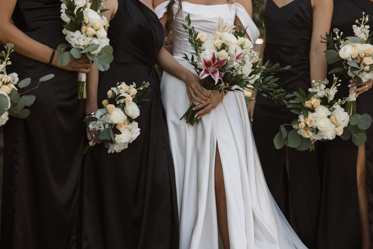 Bride and attendants holding coordinated white and cream bouquets, with pink lilies in the bridal bouquet.